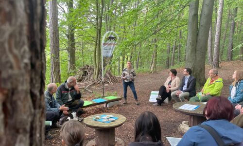 Projektstart im Wald, alle Teilnehmer sitzen im Kreis und die Geschäftsführerin begrüßt alle Anwesenden